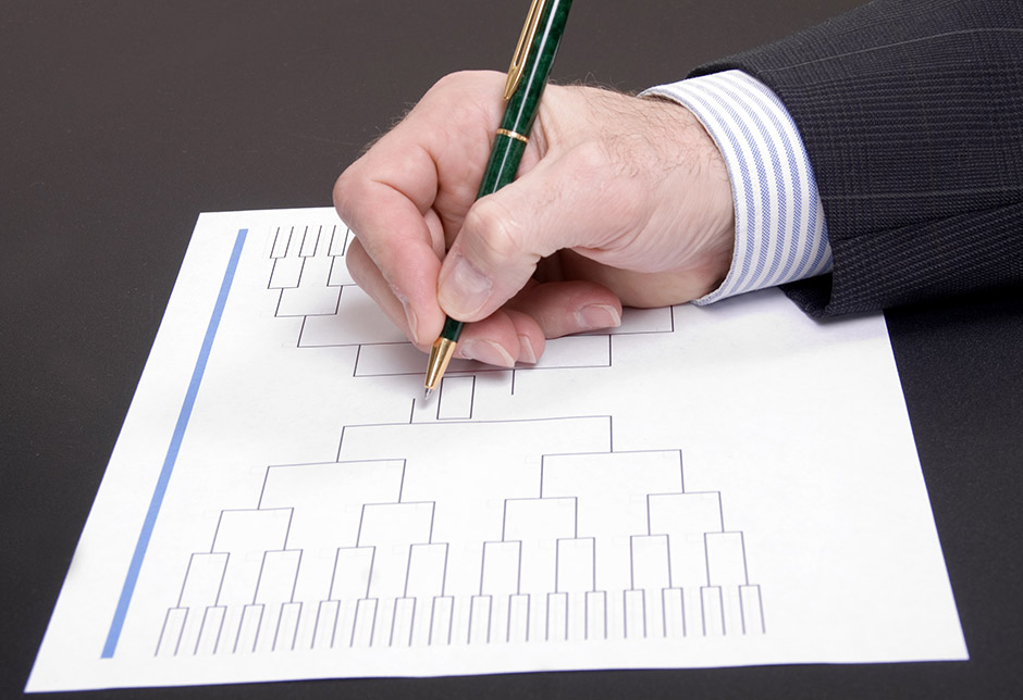 A hand holds a pen to a sheet of paper with a bracket chart printed on it